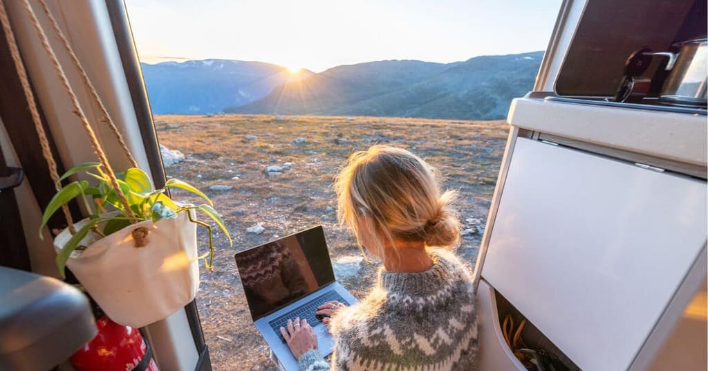 Remote worker enjoying sunrise views while working on a laptop outdoors, practicing work-life balance.