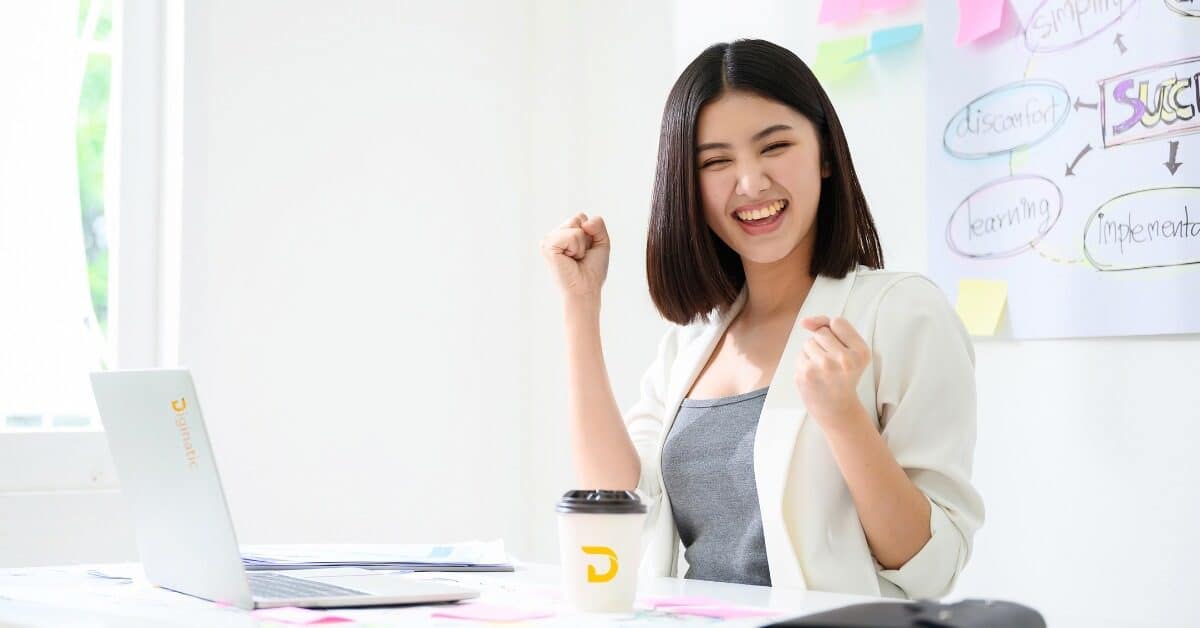 Filipina in a modern workspace celebrating a work win—symbolizing job satisfaction and positive work environment.